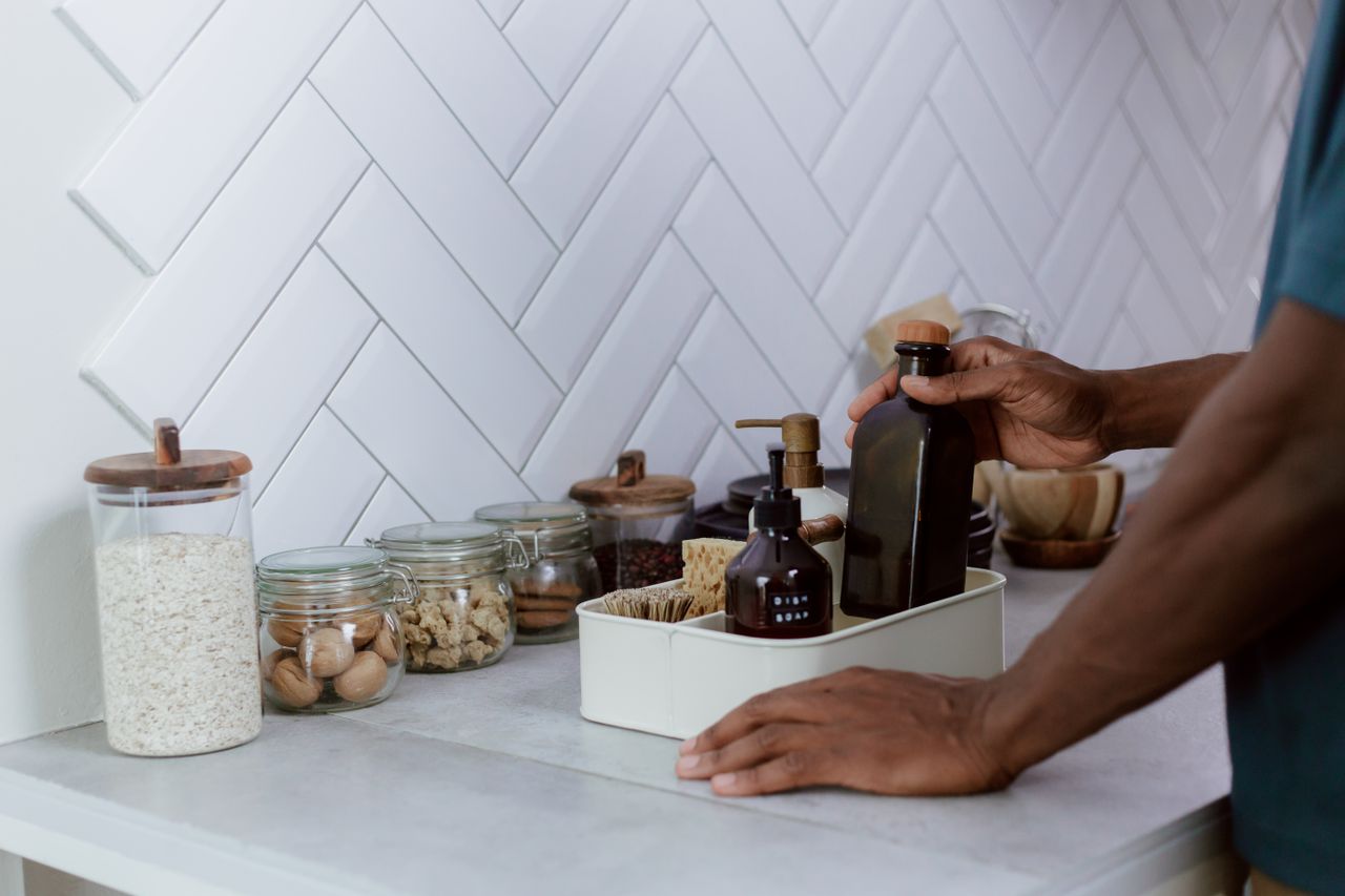 A person tidily organizes a kitchen counter with reusable glass jars and bottles.