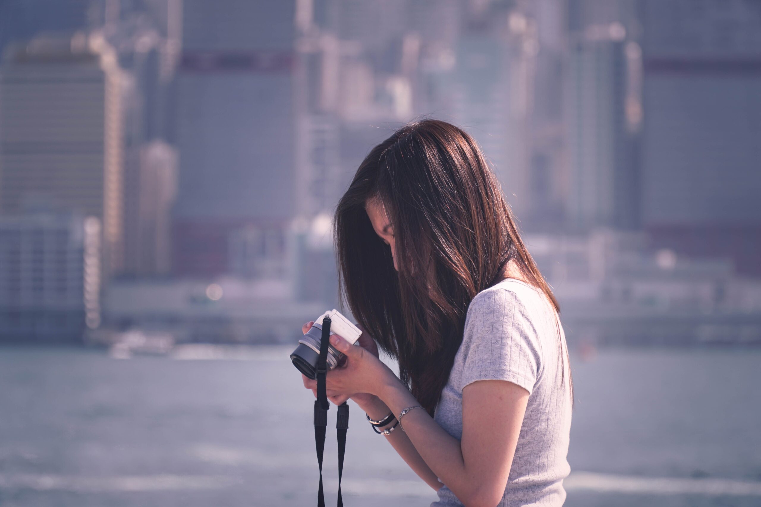 Woman with camera capturing moments against Hong Kong skyline.